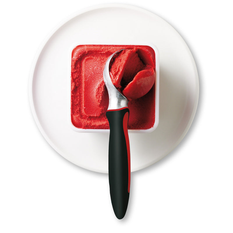 Ice cream scoop with black handle scooping red sorbet from a square container on a plate