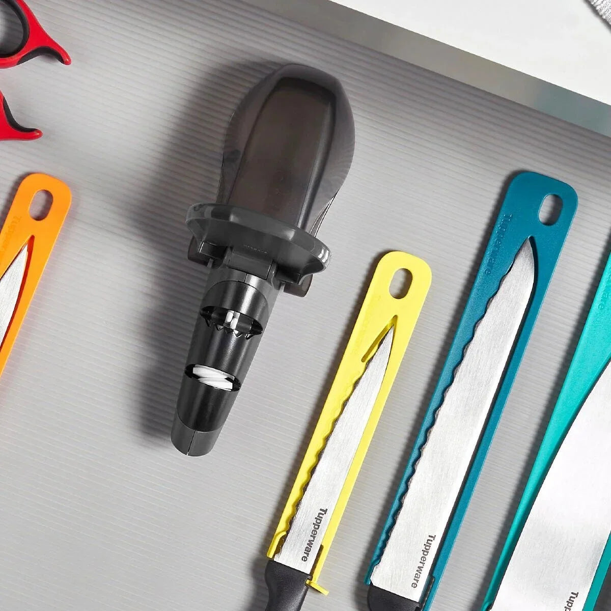 Assorted kitchen knives and a black kitchen tool on a light countertop, colorful knife sheaths