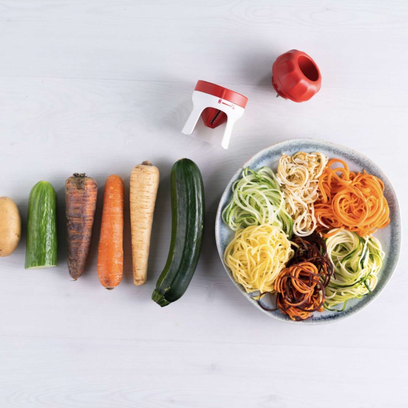 Vegetable spiralizer with raw veggies and spiralized vegetable noodles on a plate