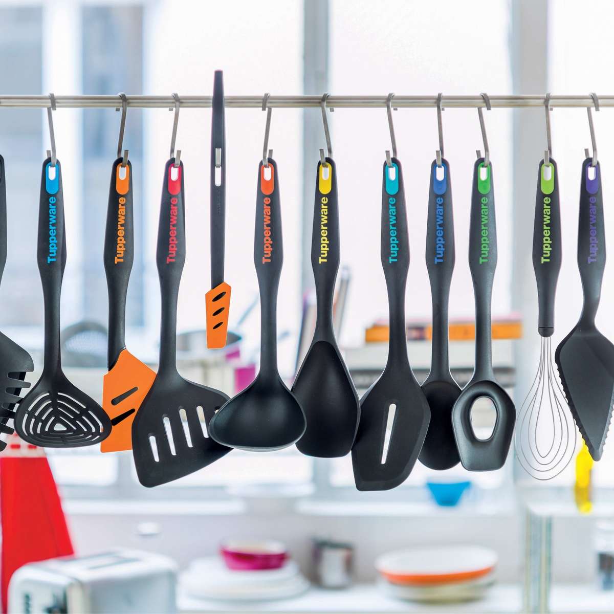 Set of colorful kitchen utensils with black handles hanging on a rack in a modern kitchen