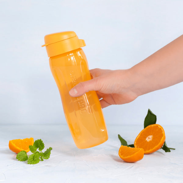 A hand holding an orange Tupperware EcoFles Plus Slim 500 ml water bottle next to orange slices.