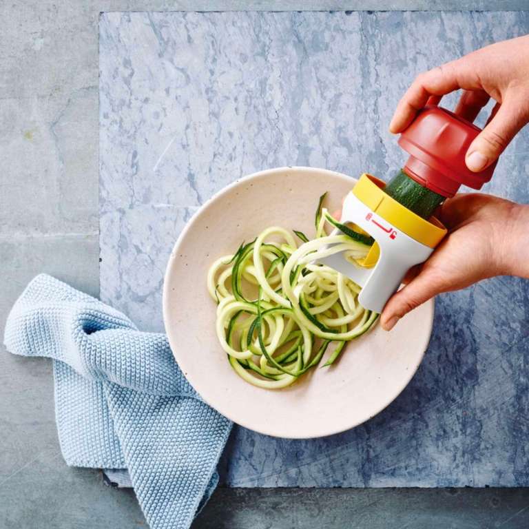 Hand spiralizing zucchini noodles with a vegetable spiralizer over a bowl
