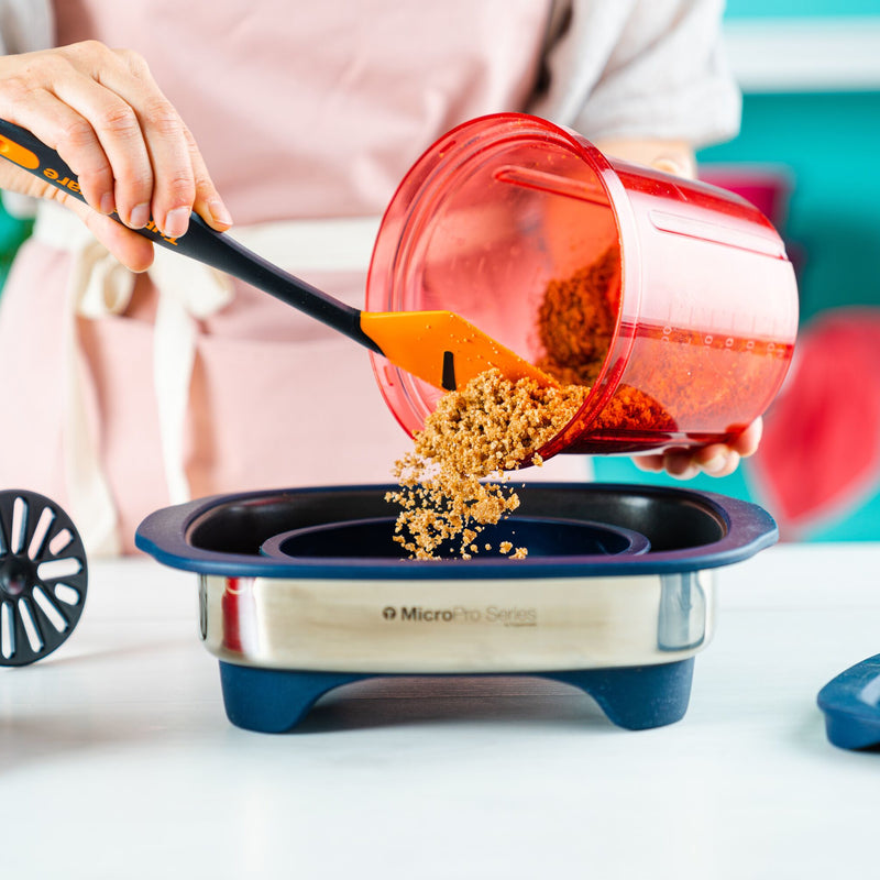Pouring breadcrumbs into a Tupperware Micro Pro Grill Ring using a red container and spatula.