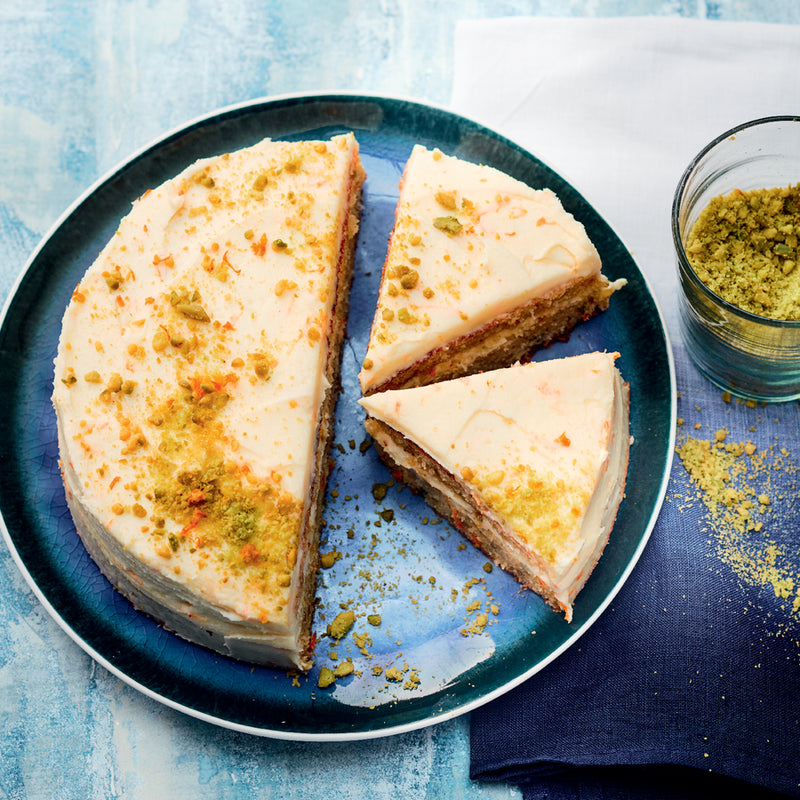 Slices of carrot cake with cream cheese frosting and pistachio crumbs on a blue plate.