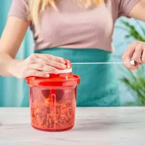 Hand using a red manual food chopper with pull cord on a kitchen counter