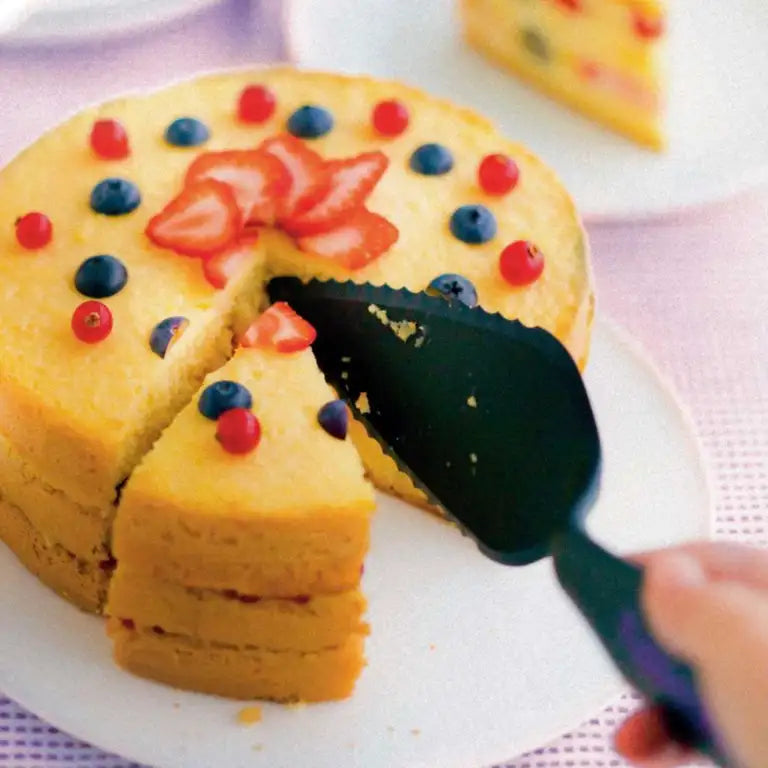 A black Tupperware cake server slicing a piece of fruit-topped cake.