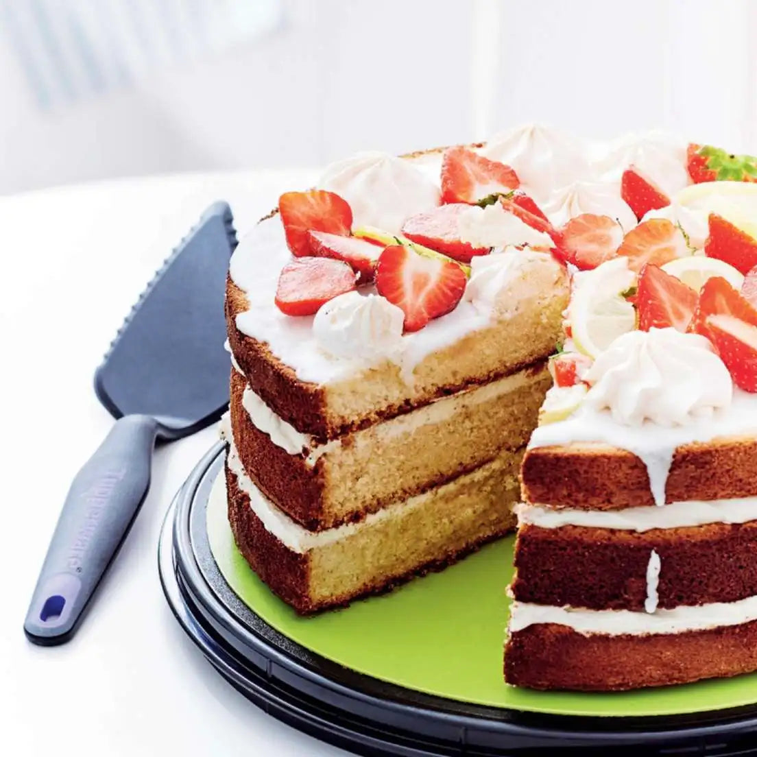 Tupperware cake server next to a sliced layer cake with strawberries and meringue