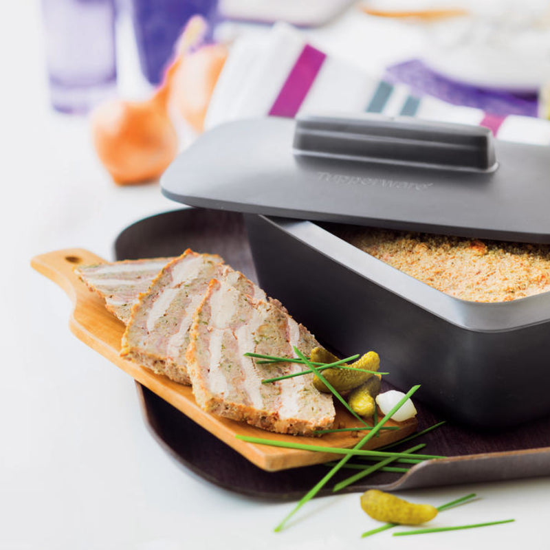 Sliced meatloaf on a wooden board next to a Tupperware UltraPro Terrine dish