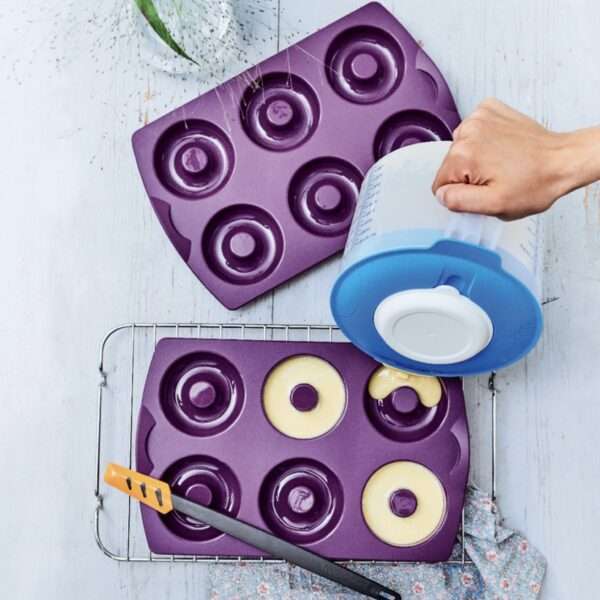 Purple silicone donut baking molds filled with batter on a cooling rack, kitchen utensil visible