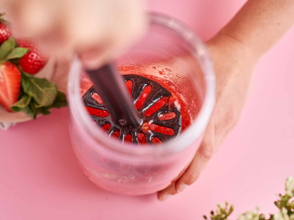 Hand gebruikt keukenhulpmiddel om aardbeien te mengen in glas, perfect voor smoothies en frisse dranken