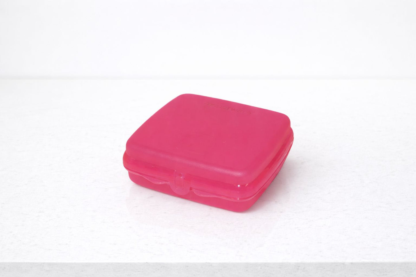 Pink plastic sandwich box on a white countertop for kitchen storage
