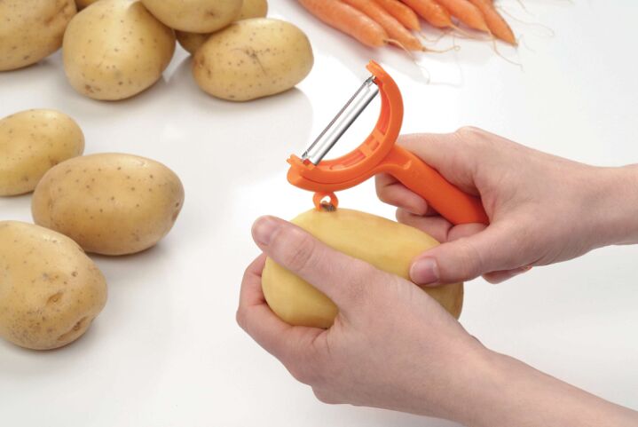 Oranje schilmesje gebruiken voor aardappelschillen, met verse aardappelen en wortels op achtergrond