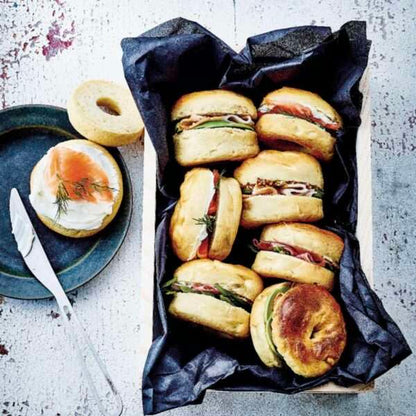 Assorted mini bagel sandwiches with smoked salmon, cream cheese, and fresh herbs in a wooden tray