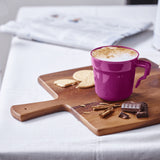 Purple coffee mug with cappuccino on wooden cutting board, biscuits and chocolate pieces