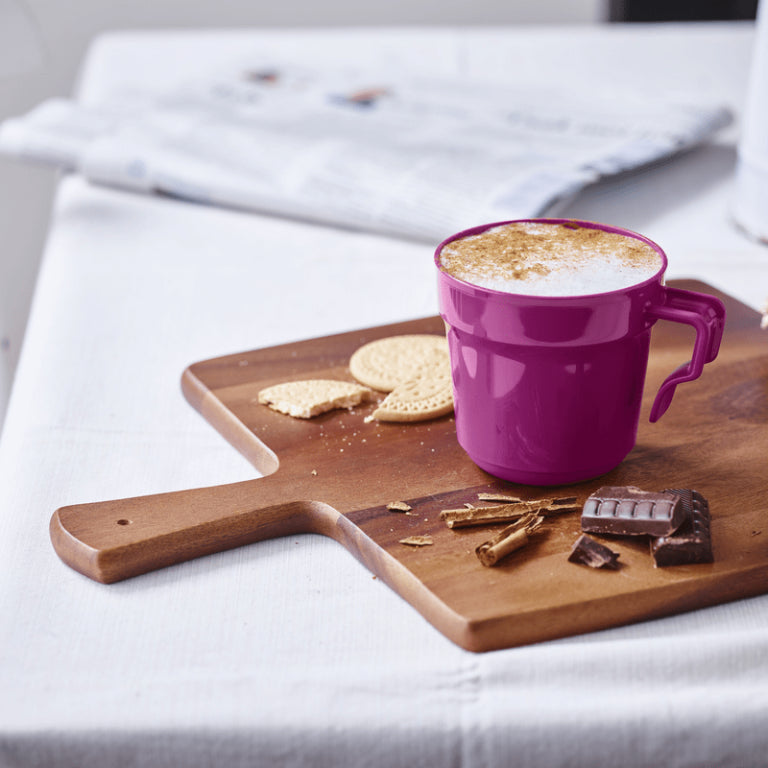 Purple coffee mug with cappuccino on wooden cutting board, biscuits and chocolate pieces