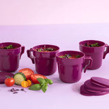 Set of four purple soup mugs with handles and lids, fresh vegetables in foreground on a light surface