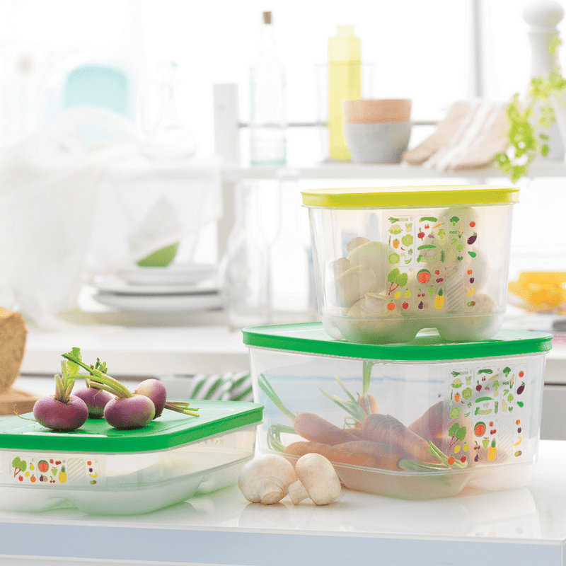 Plastic food storage containers with green lids holding fresh vegetables in a bright kitchen