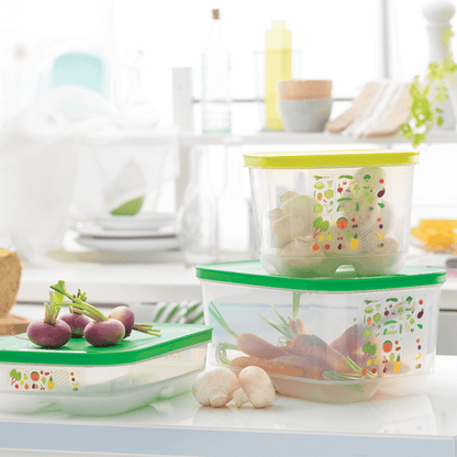 Plastic food storage containers with green lids holding fresh vegetables in a bright kitchen