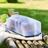Transparante broodtrommel met brood op houten bank in tuin, ideaal voor picknicks en buitenkoken