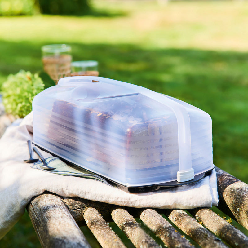 Transparante broodtrommel met brood op houten bank in tuin, ideaal voor picknicks en buitenkoken