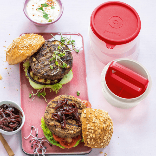 Smakelijke hamburgers met groenten en sauzen op roze bord, naast rode opbergdozen voor keukentools