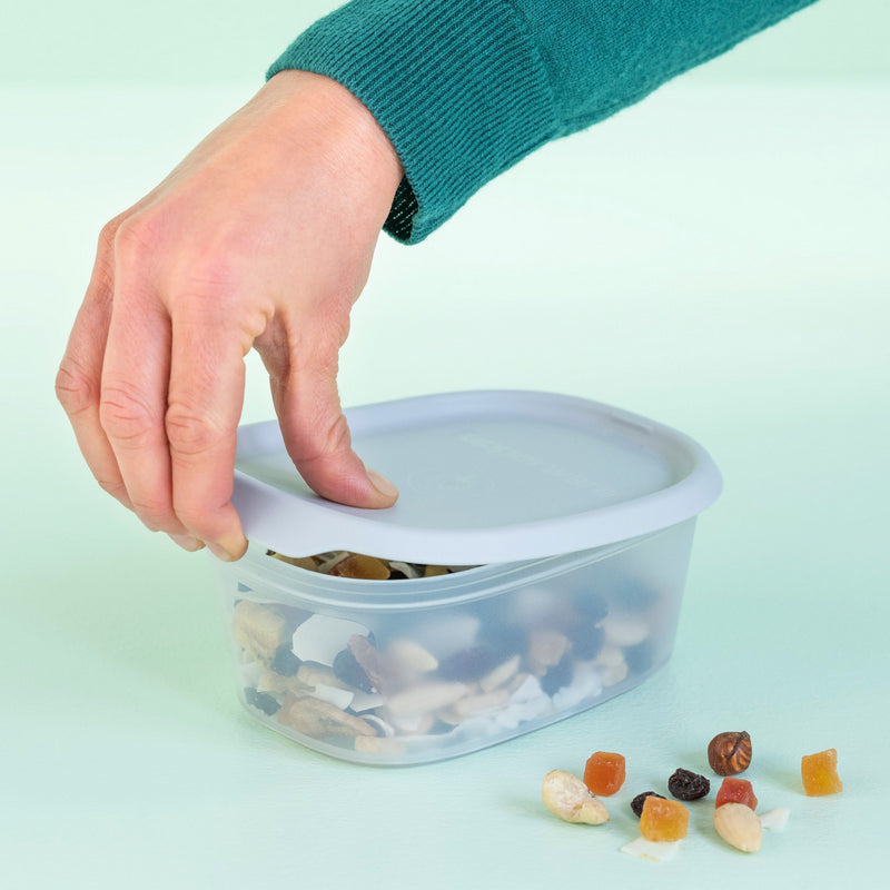 Hand opent transparante opbergdoos met noten en gedroogd fruit, ideaal voor keukenorganisatie