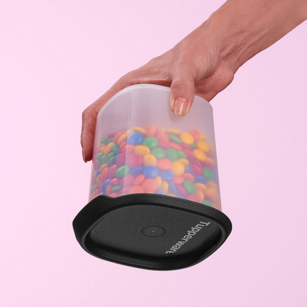 Hand holding a plastic food storage container with colorful candy and a black lid