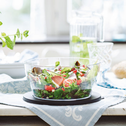 Glass salad bowl filled with fresh greens and vegetables on a kitchen table