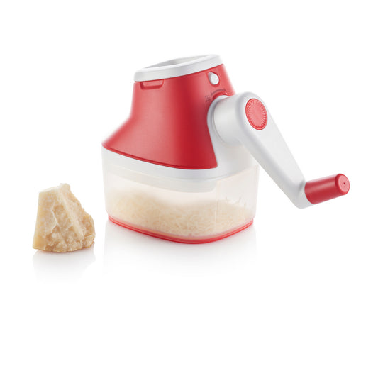 Handheld cheese grater with red handle and container, next to a block of cheese on white background