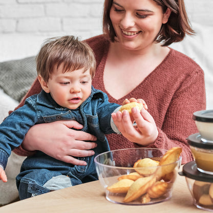 Mother and child sharing baked snacks from a clear bowl, food storage containers nearby