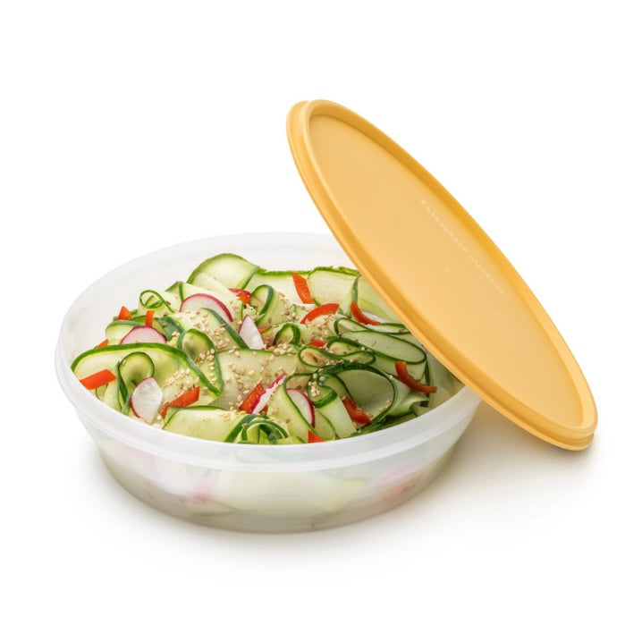 Round plastic food storage container with yellow lid, filled with fresh vegetable salad