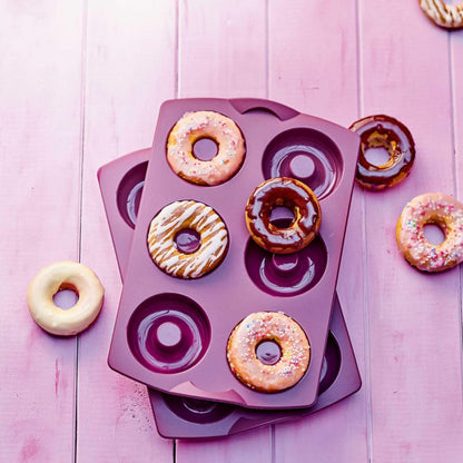 Purple silicone donut baking molds with decorated donuts on pink wooden surface