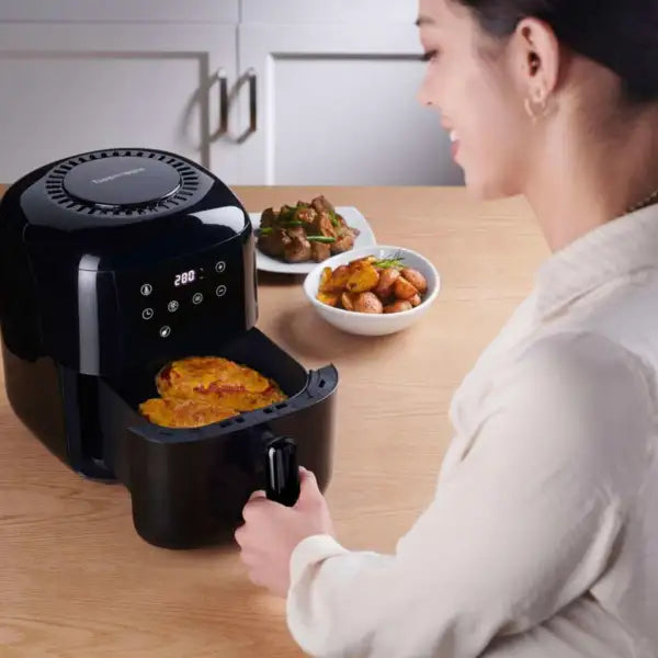 Woman using a digital air fryer in kitchen with cooked food on countertop