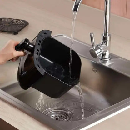 Hand washing a black air fryer basket in a modern kitchen sink under running water