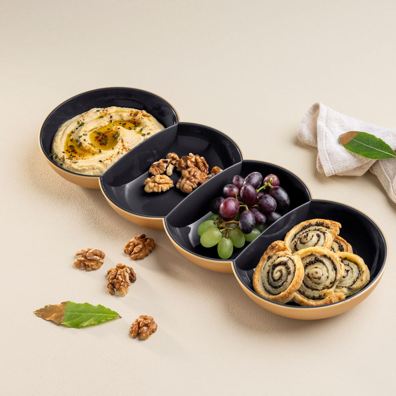 Black and gold Tupperware divided serving bowl with hummus, walnuts, grapes, and pinwheels