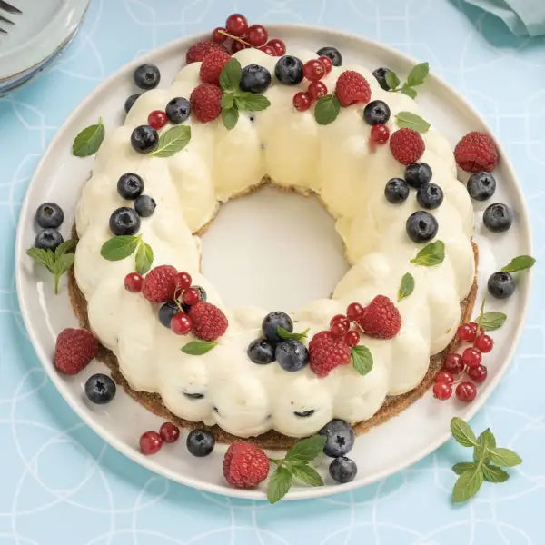 Ring-shaped pudding dessert topped with fresh raspberries, blueberries, red currants, and mint leaves on a white plate.