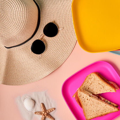 Zomerse picknick met sandwich op roze bord, strooien hoed, zonnebril en schelpen op roze achtergrond