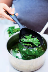 Black slotted spoon lifting green peas and snap peas from a pot of boiling water