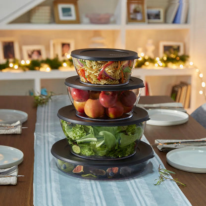 Stacked clear salad bowls with black lids filled with fresh food on a dining table
