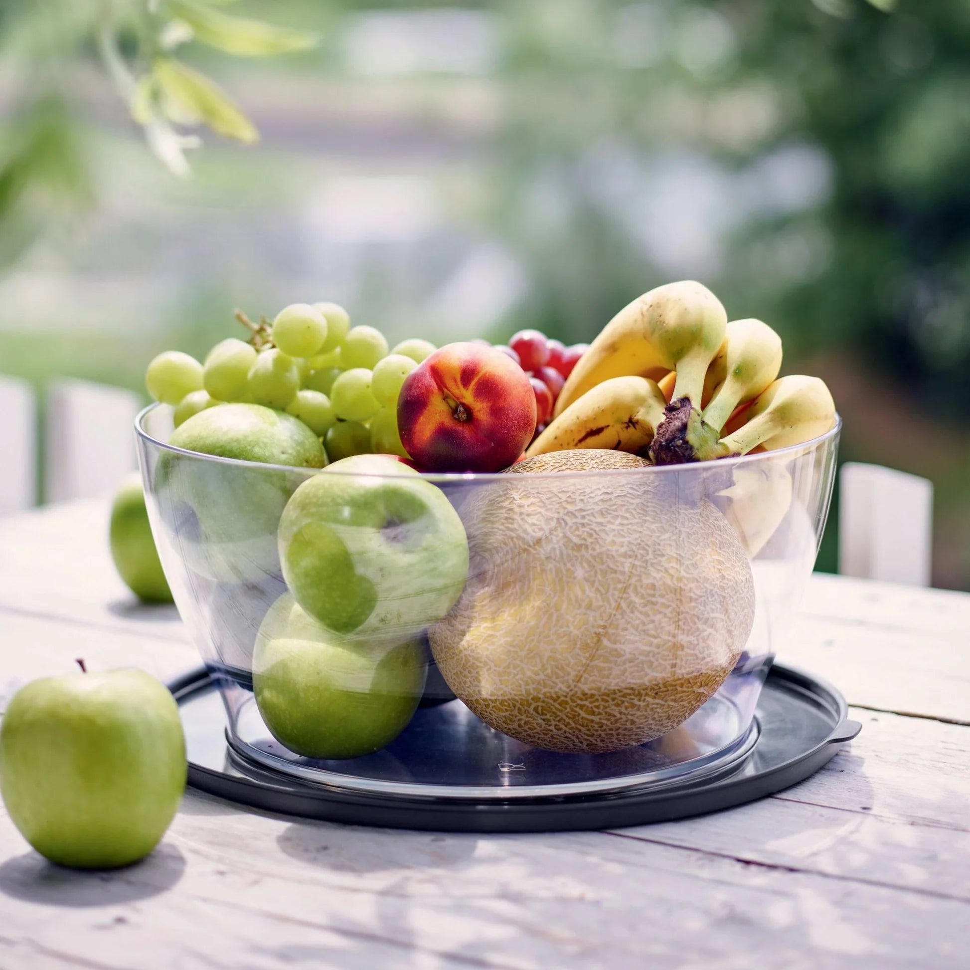 Transparent salad bowl filled with fresh fruit on a wooden table outdoors