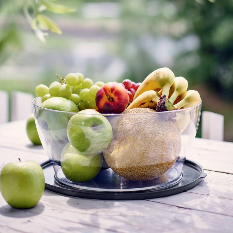 Transparent salad bowl filled with fresh fruit on a wooden table outdoors