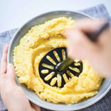 Hand gebruikt aardappelpuree maker voor gladde puree in een kom