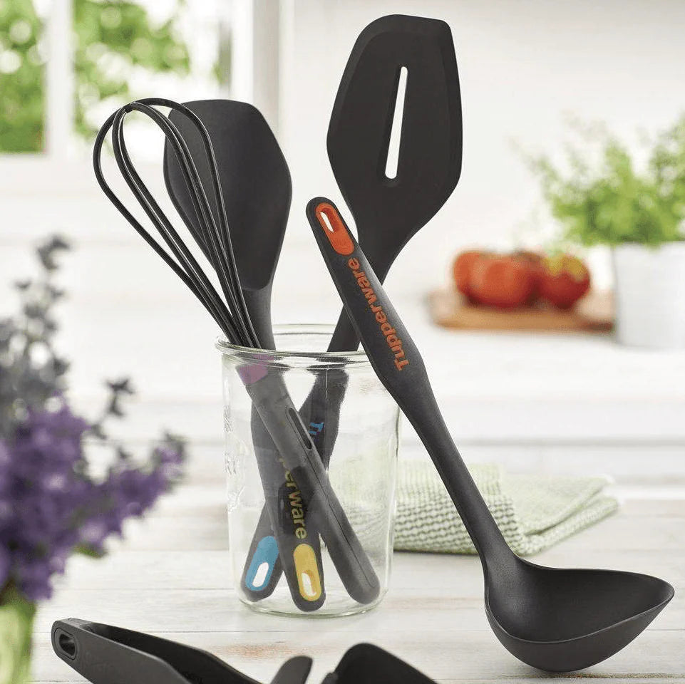 Black kitchen utensils including ladle, whisk, and spatula in a glass jar on a kitchen counter