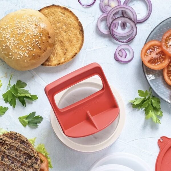 Rode hamburgerpress voor perfecte patties, omringd door buns, ui en tomaat
