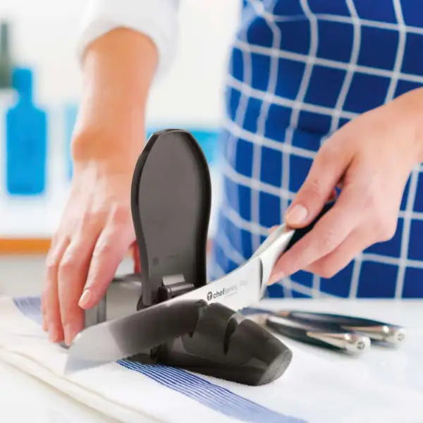 Person sharpening kitchen knife with a manual knife sharpener on countertop