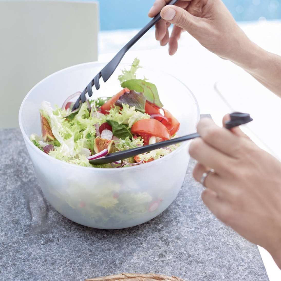 Zwarte salade tongs gebruikt om verse groenten te mengen in een transparante kom