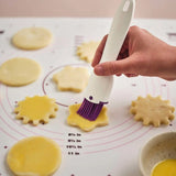 Hand brushing egg wash on raw cookie dough with a silicone pastry brush on baking mat