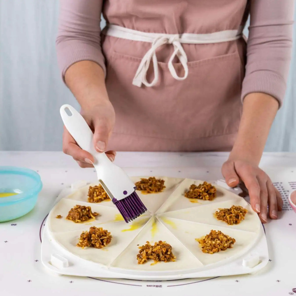 Woman using silicone pastry brush to apply egg wash on dough wedges with savory filling