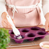 Woman brushing purple silicone muffin pan with pastry brush in kitchen