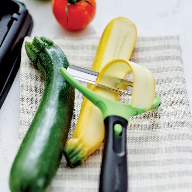 Groene en gele courgette met groenten schilmes op gestreept keukentextiel, perfect voor culinaire gerechten